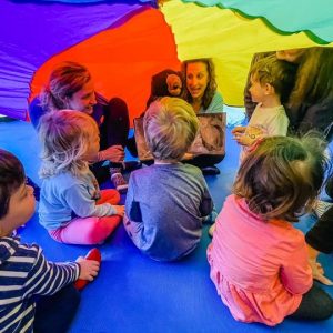 teacher reads a story to kids under a colorful parachute