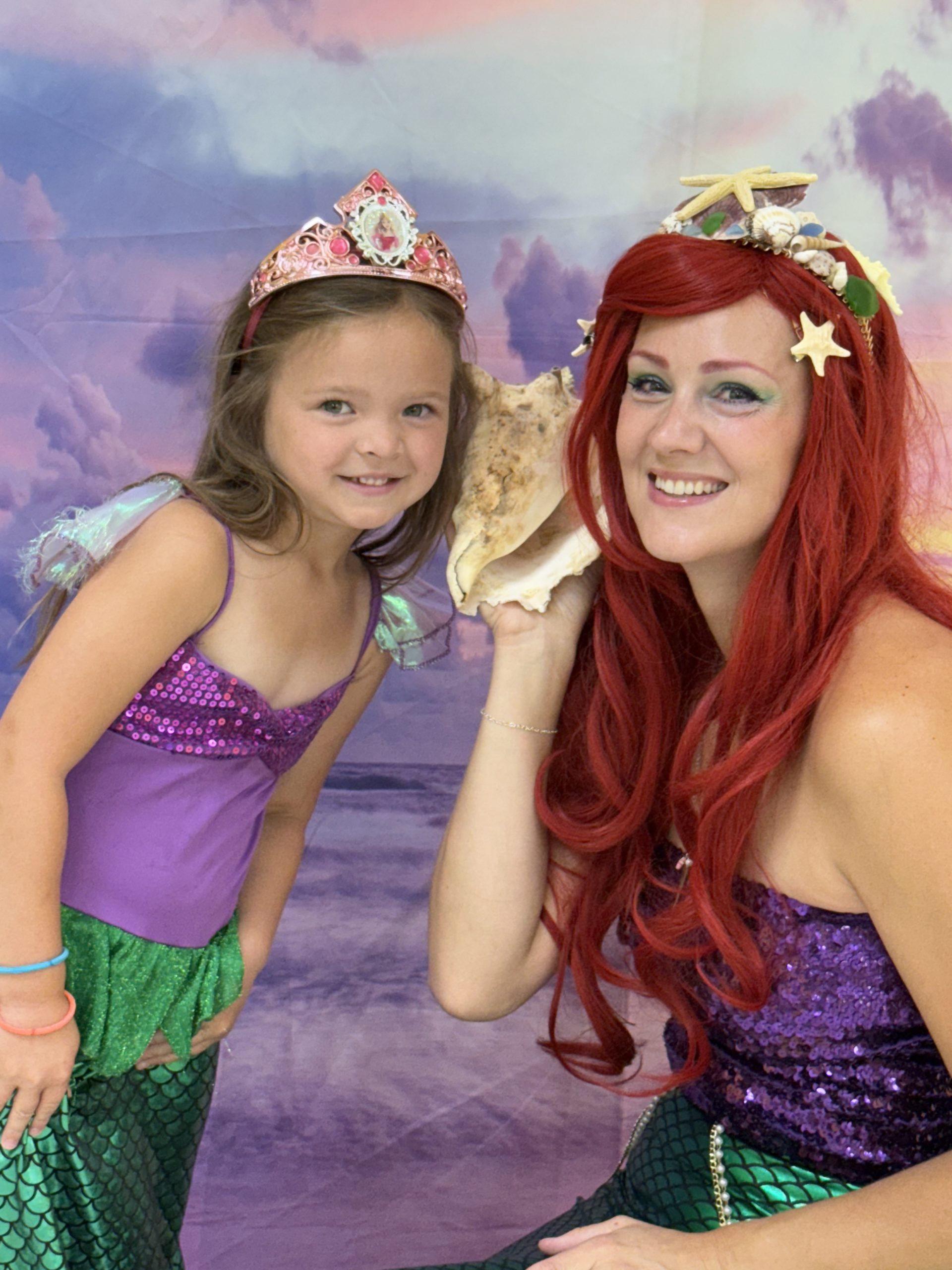 Red-headed mermaid and young girl listen to sea shell during Fun Friday at The Playroom in Forest Hill