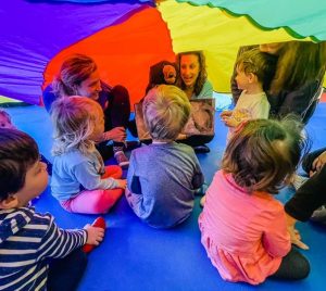 teacher reads a story to kids under a colorful parachute